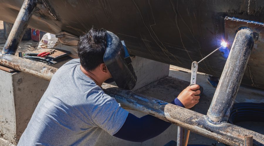 A welder is welding base stand of the old large oil tank to be renovated for a water tank